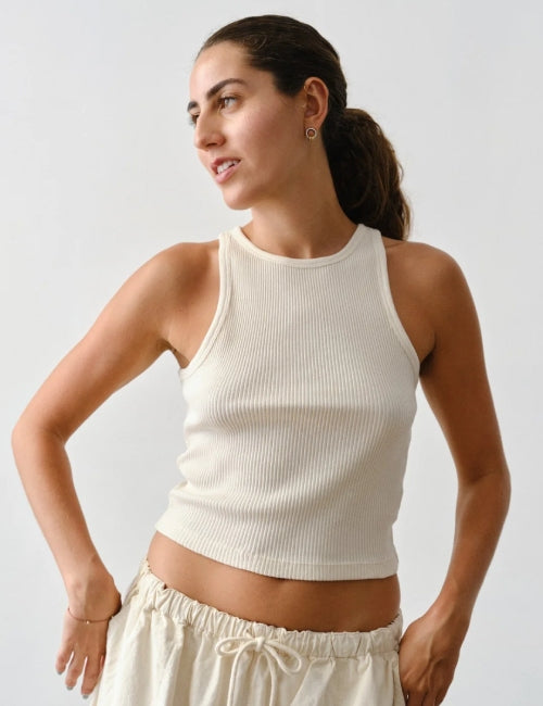 A woman wearing a ribbed cream-colored sleeveless crop top and matching cream drawstring pants, photographed against a plain light gray studio background.