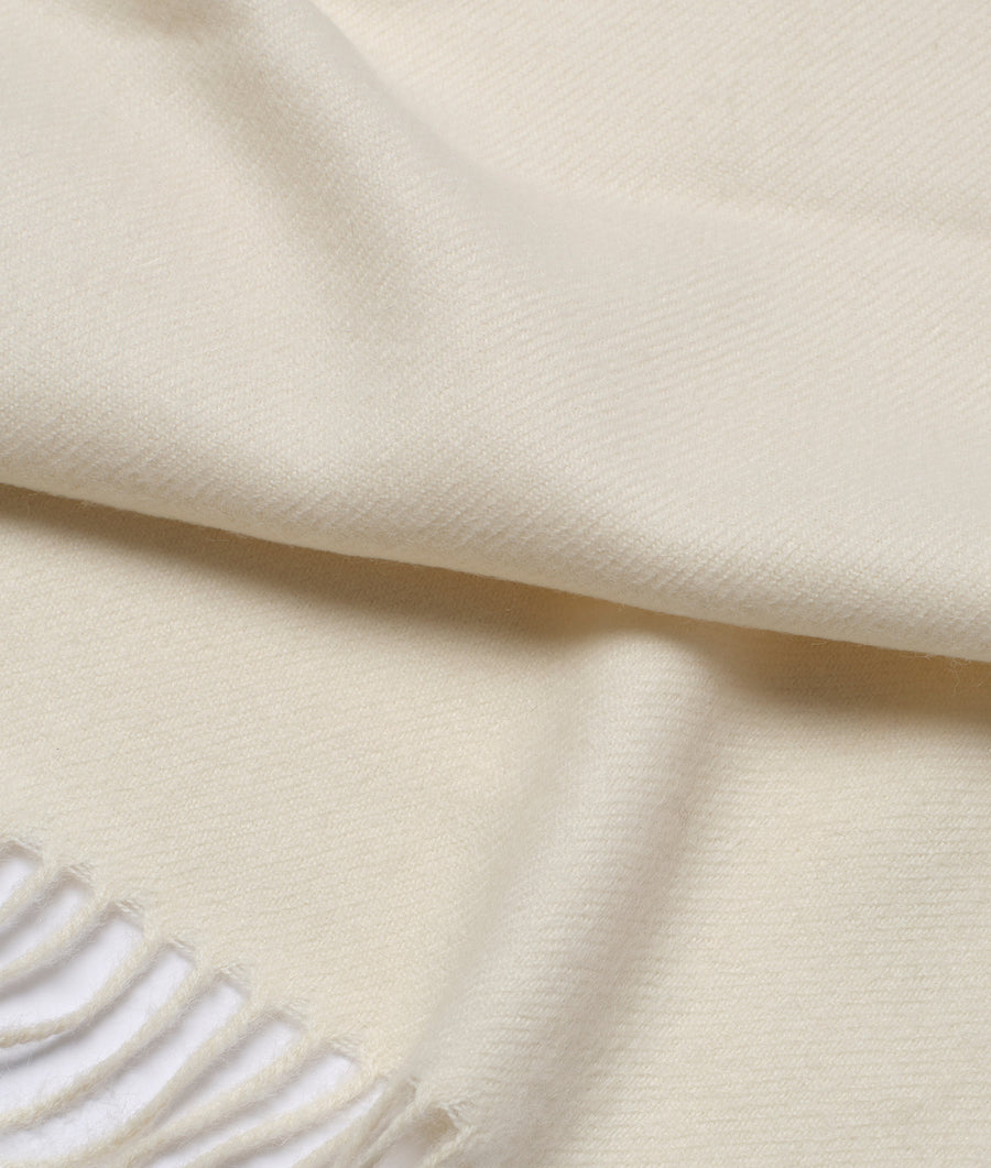 Flat lay of a cream-colored organic cotton scarf with fringed edges - Industry of All Nations