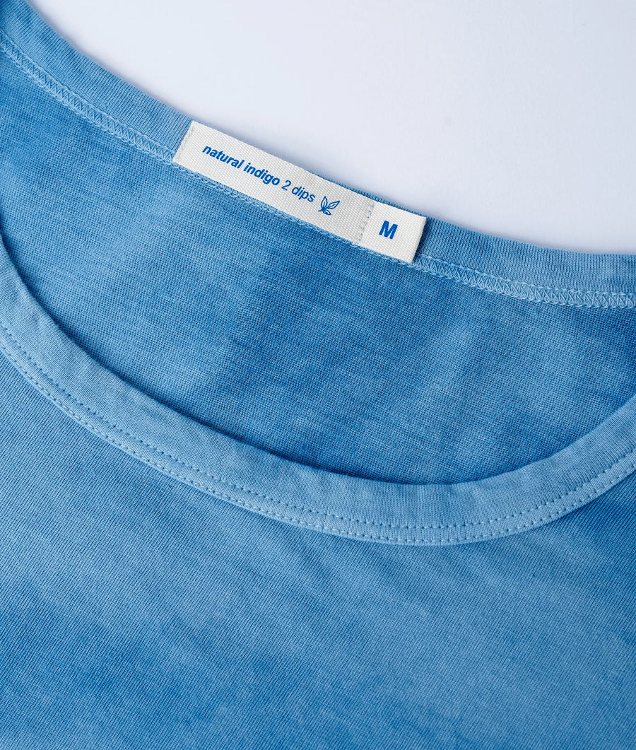 Close-up detail shot of a light blue organic cotton t-shirt with 'natural indigo 2 dips' label - Industry of All Nations