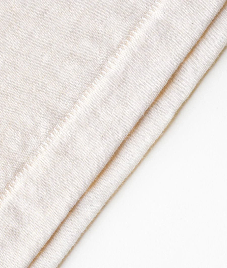 Flat lay shot of a white organic cotton long-sleeve top with subtle diagonal stitching detail - Industry of All Nations