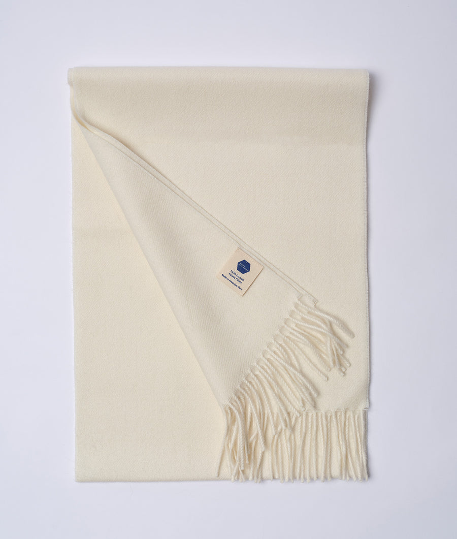 A white alpaca scarf in a flat lay display with fringe ends and a woven label - Industry of All Nations