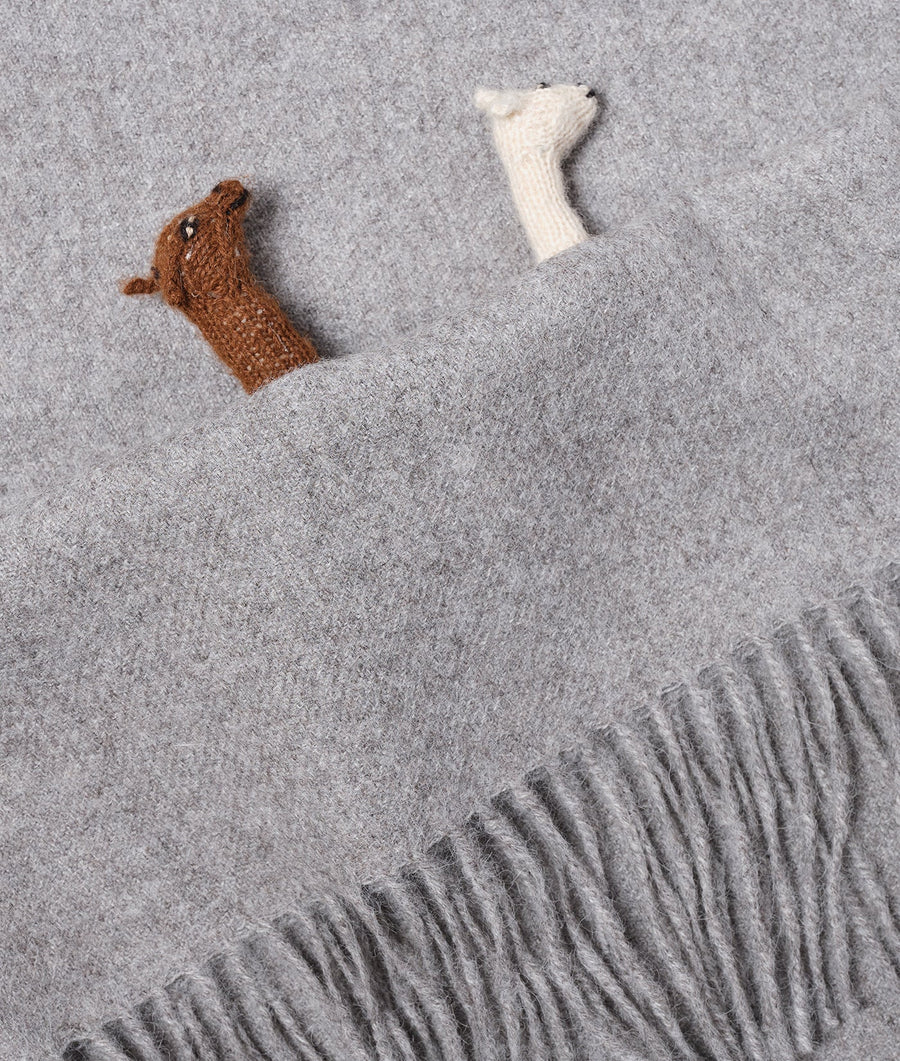 A grey, woolen blanket or shawl with fringe and a small, brown knitted toy resting on it - Industry of All Nations