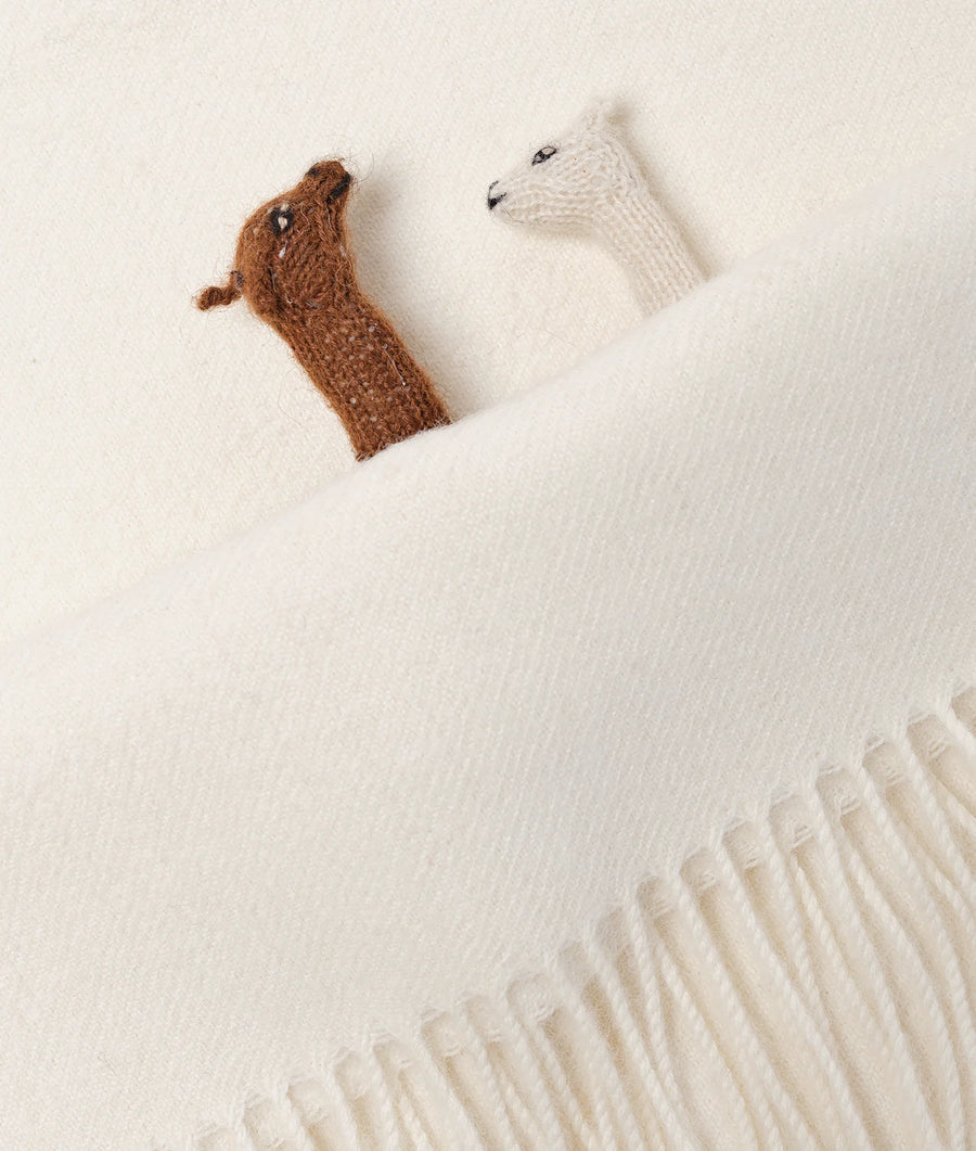 Flat lay image of a beige knit scarf with two crocheted animal figures, one brown and one white - Industry of All Nations