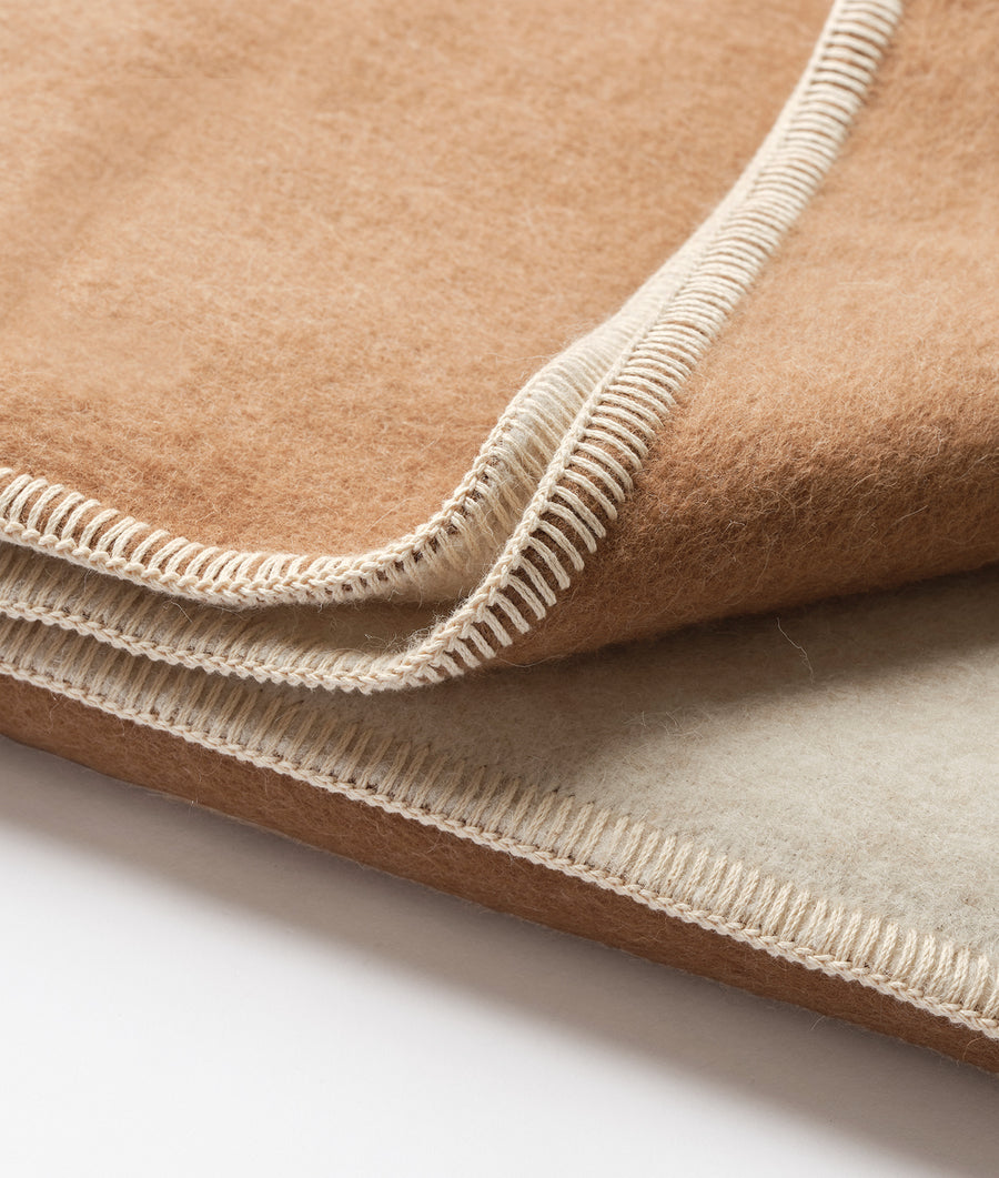 Close-up of a beige wool blanket with a decorative woven edge detail - Industry of All Nations