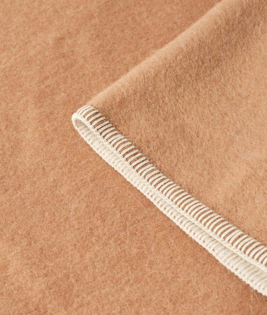 A close-up detail shot of the tan, woven trim on the sleeve of a camel-colored wool garment - Industry of All Nations
