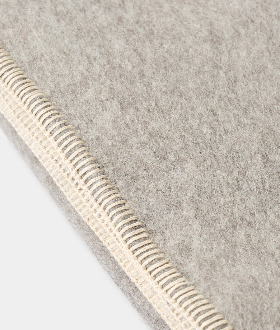 Flat lay detail of a light gray woven alpaca blanket with ivory stitching along the edge - Industry of All Nations