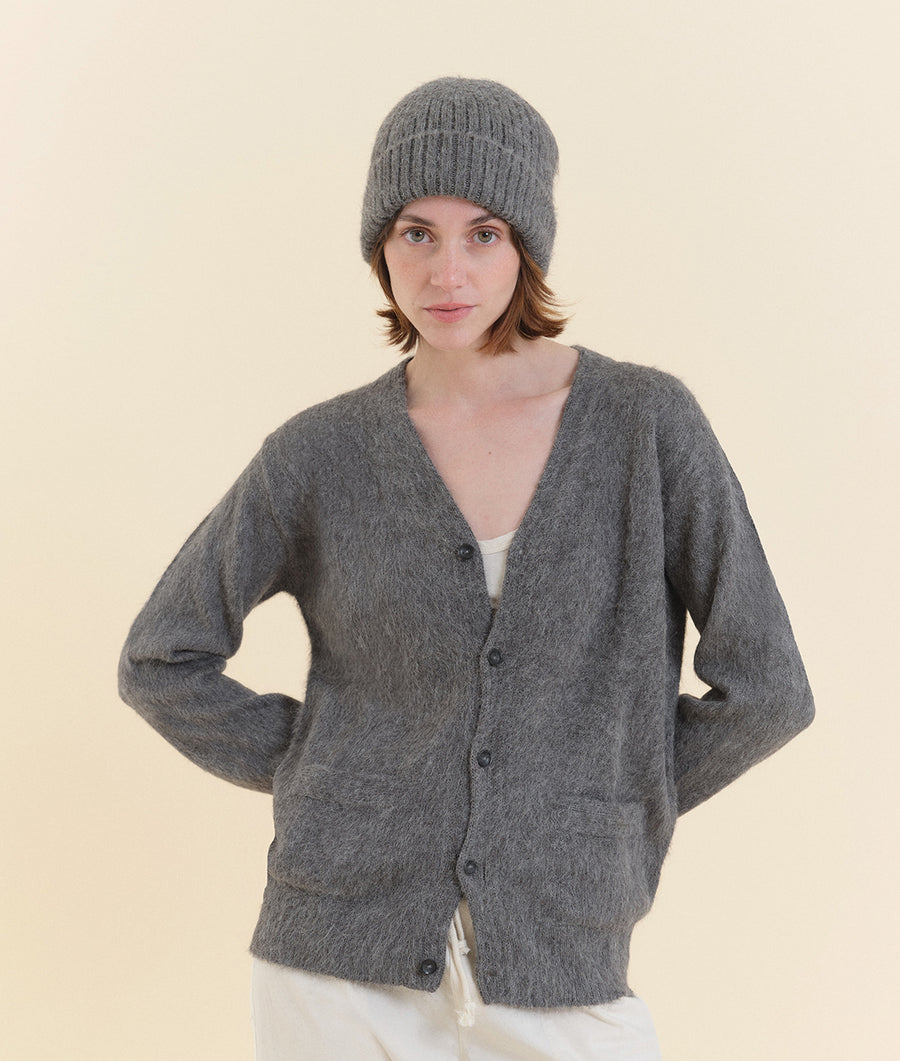 A woman wearing a gray wool cardigan with pockets, standing against a light-colored background - Industry of All Nations