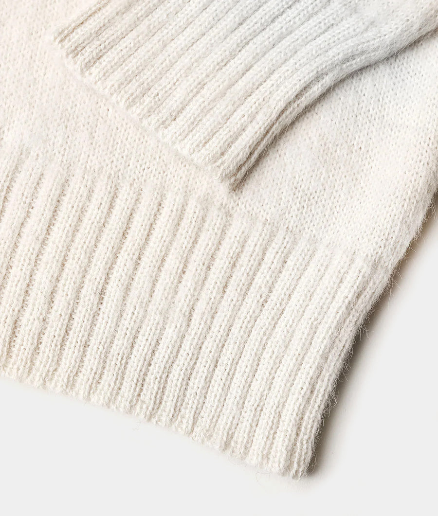 Closeup of a white, hand-knit alpaca scarf with textured stripes and tassels displayed flat on a plain background - Industry of All Nations
