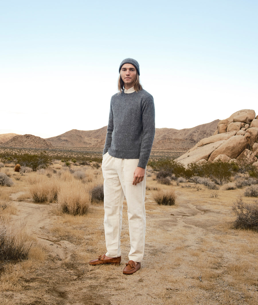Gray knitted sweater and cream-colored pants worn by a person standing in a desert landscape - Industry of All Nations