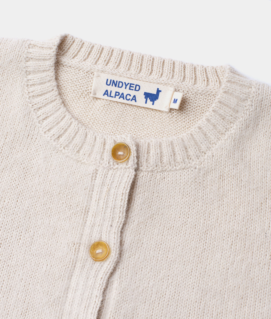 Detail shot of a beige alpaca sweater with a ruffle collar and large yellow buttons, displaying the 'Undyed Alpaca' logo tag - Industry of All Nations