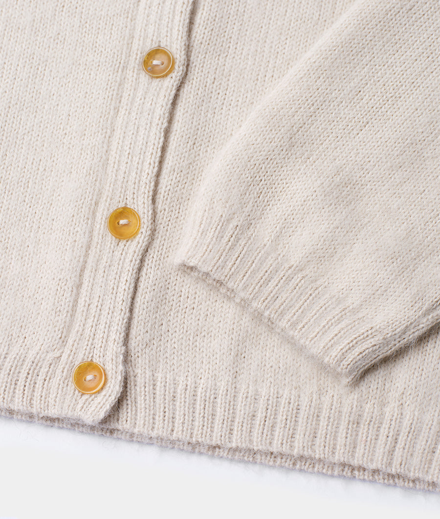 Closeup of a beige knitted cardigan with yellow buttons, displayed flat - Industry of All Nations