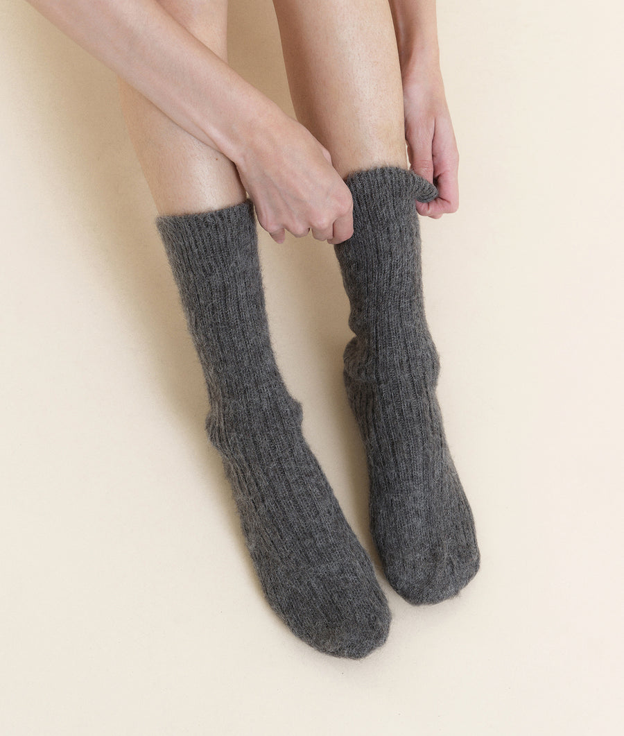 A close-up image of a pair of gray woolen socks worn on a person's legs against a light beige background. - Industry of All Nations