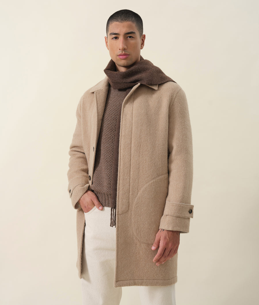A man wearing a beige wool coat with a large collar, standing against a light background - Industry of All Nations