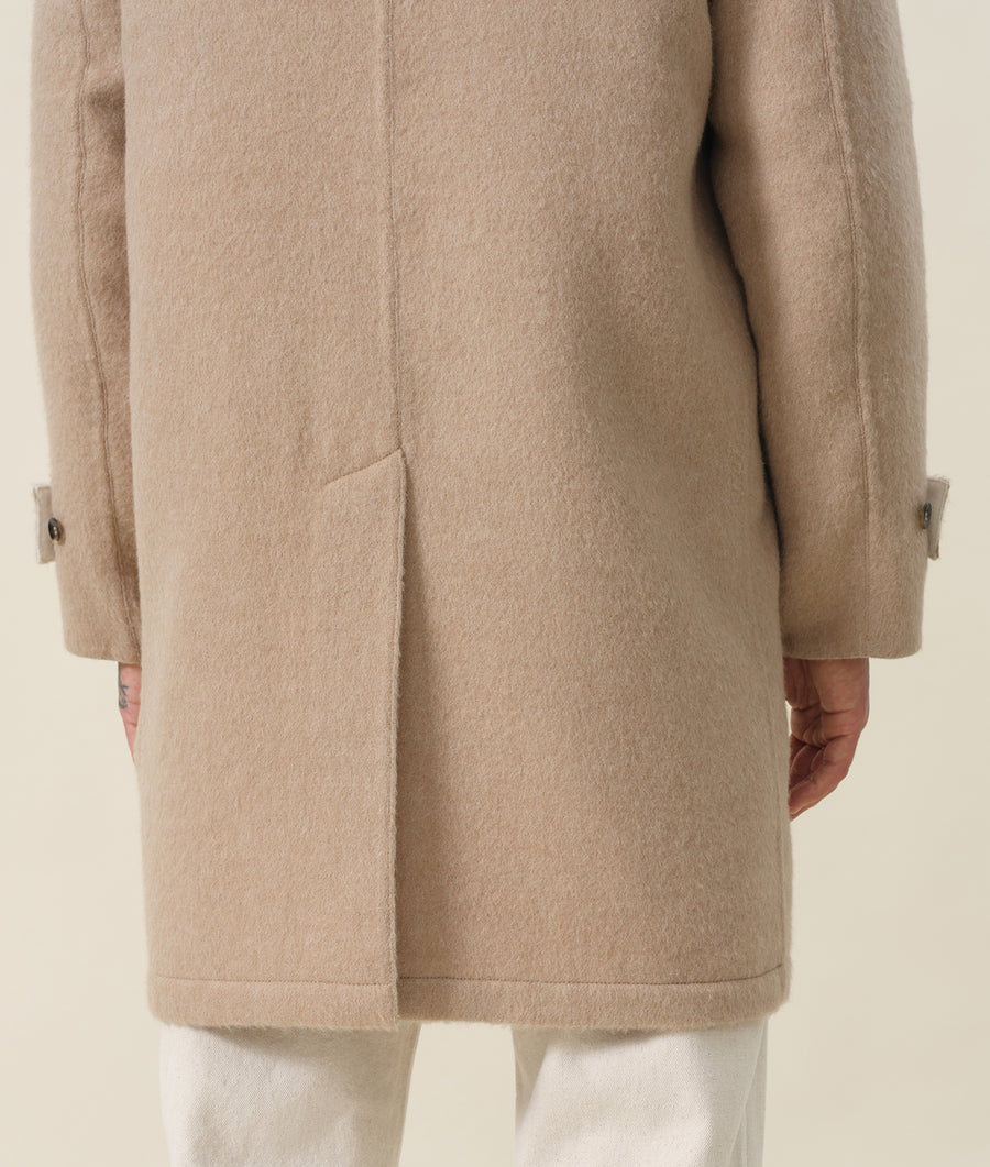 A close-up detail shot of a beige wool coat with buttons and pockets, displayed on a model - Industry of All Nations