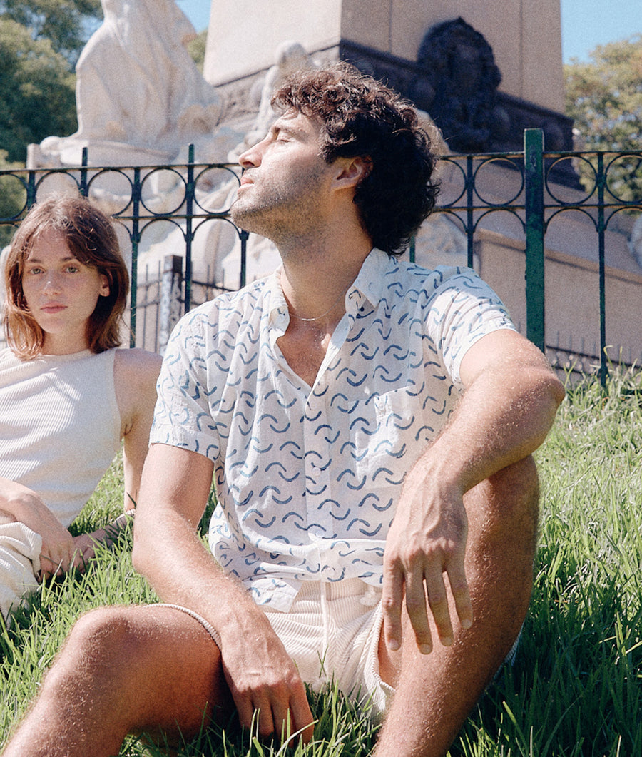 Two people sitting on grass, one wearing a patterned short-sleeved shirt - Industry of All Nations