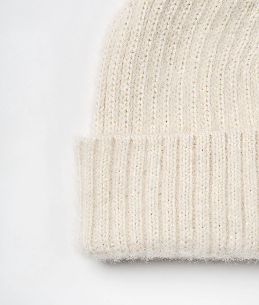 Flat lay of a cream-colored, ribbed-knit beanie or cap with a rolled hem - Industry of All Nations
