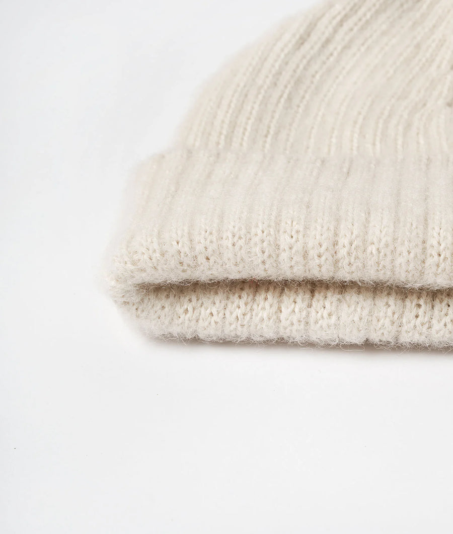 Close-up detail shot of a beige knitted alpaca scarf or wrap, folded and displayed on a white background - Industry of All Nations