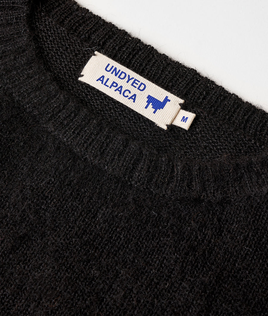 A close-up detail shot of a black knitted sweater or pullover with a sewn-in label that reads "UNDYED ALPACA" - Industry of All Nations