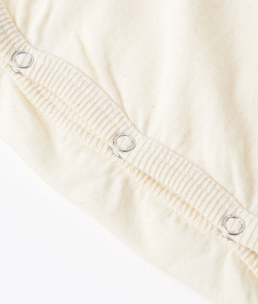 Detail shot of a white organic cotton jumpsuit with metal snap closures - Industry of All Nations