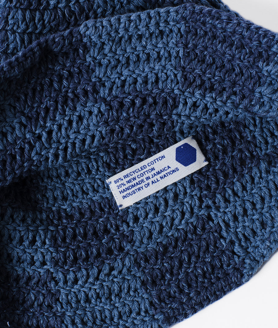 Close-up detail shot of a dark blue crocheted hat with a sewn-in label indicating it is made from 80% recycled cotton - Industry of All Nations