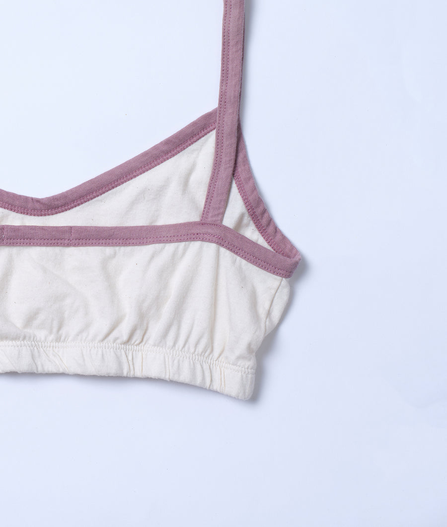 Close-up of the front panel and strap details of a white sports bra or crop top with a dusty pink trim - Industry of All Nations
