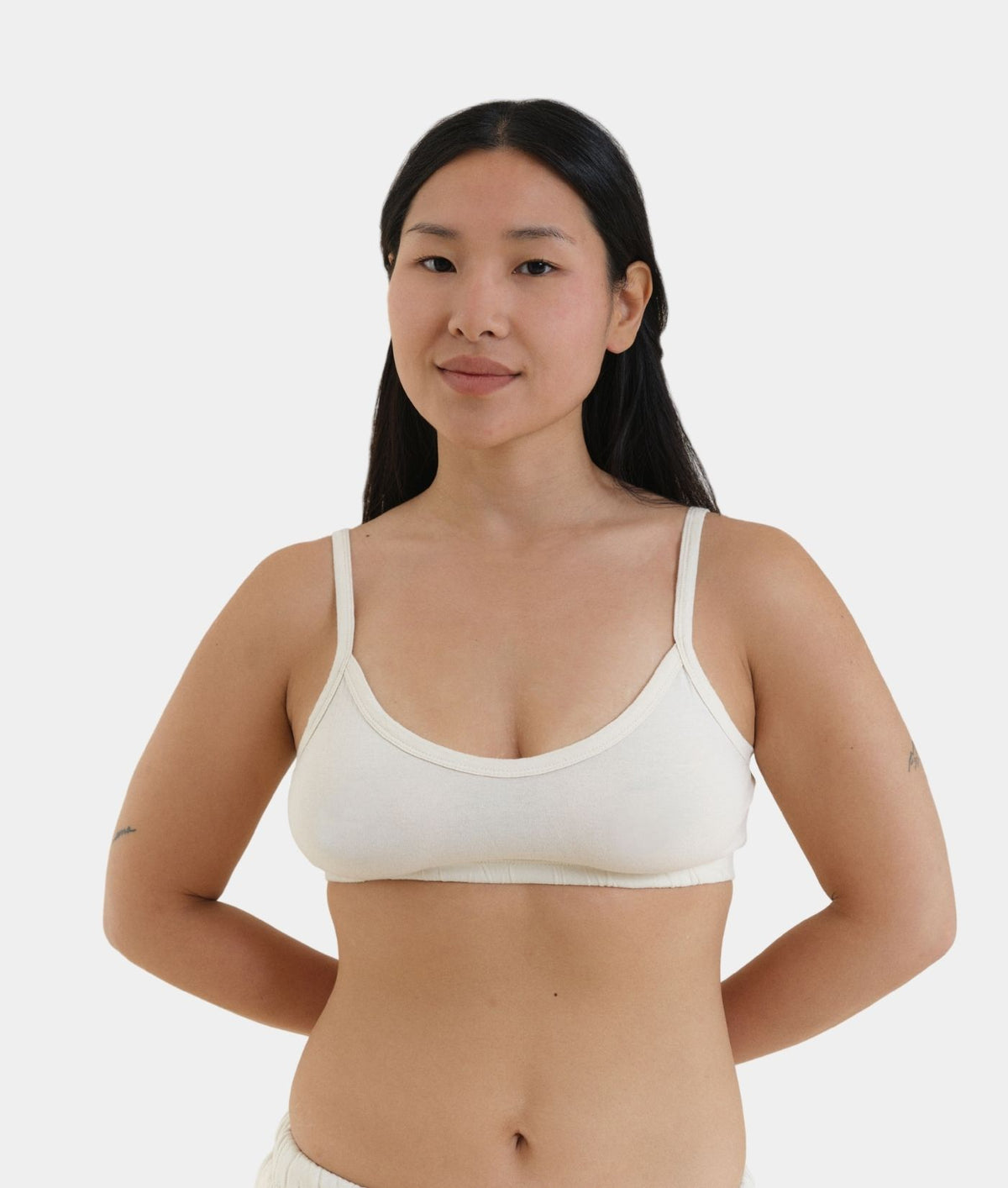 A woman modeling a cream-colored, scoop-neck bralette against a plain light gray background.