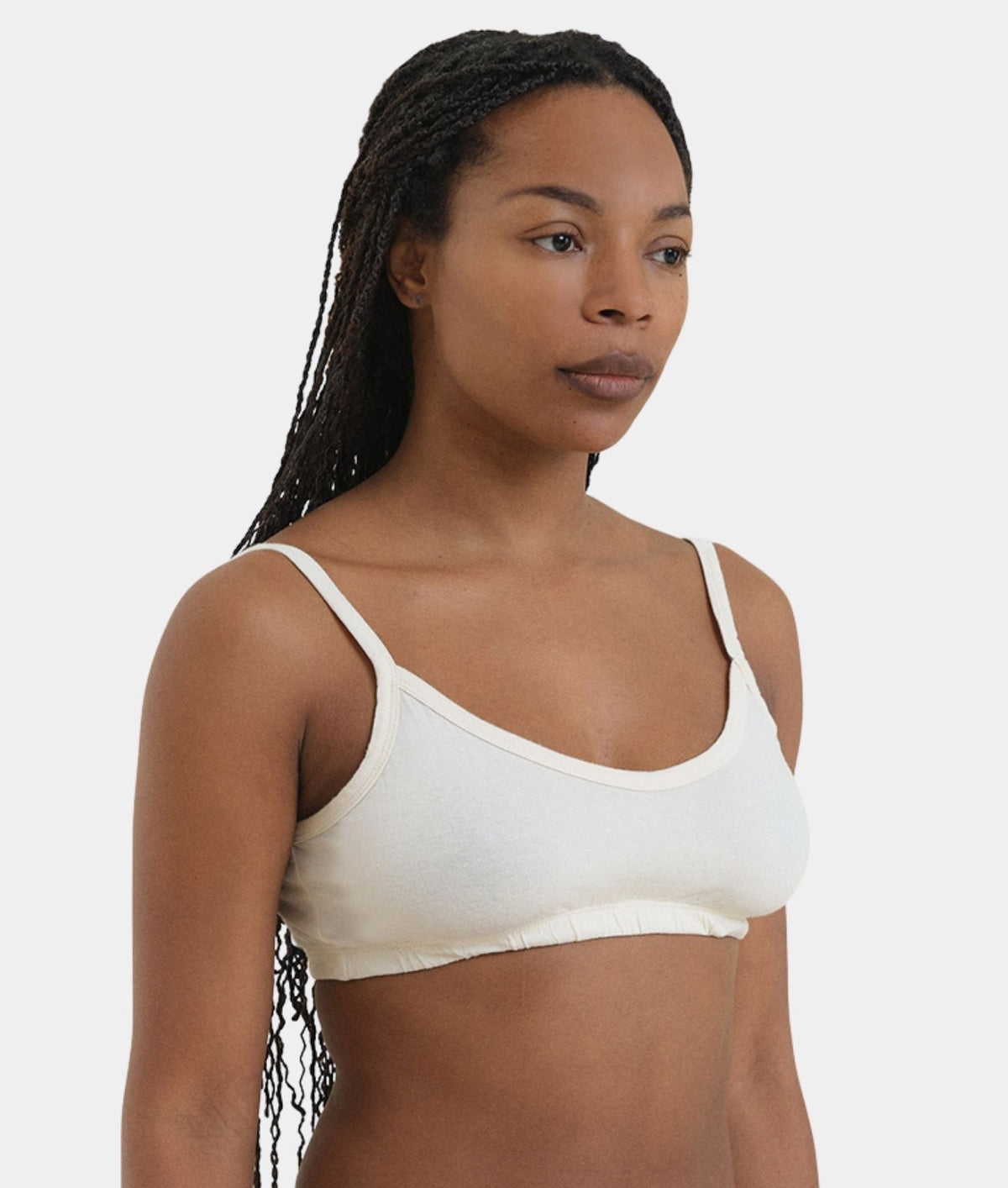 A woman wearing a white ribbed scoop-neck camisole bralette, shown from the chest up against a light gray studio background.