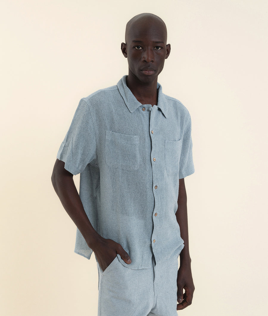 A man wearing a light blue short-sleeved button-down shirt in a studio setting - Industry of All Nations