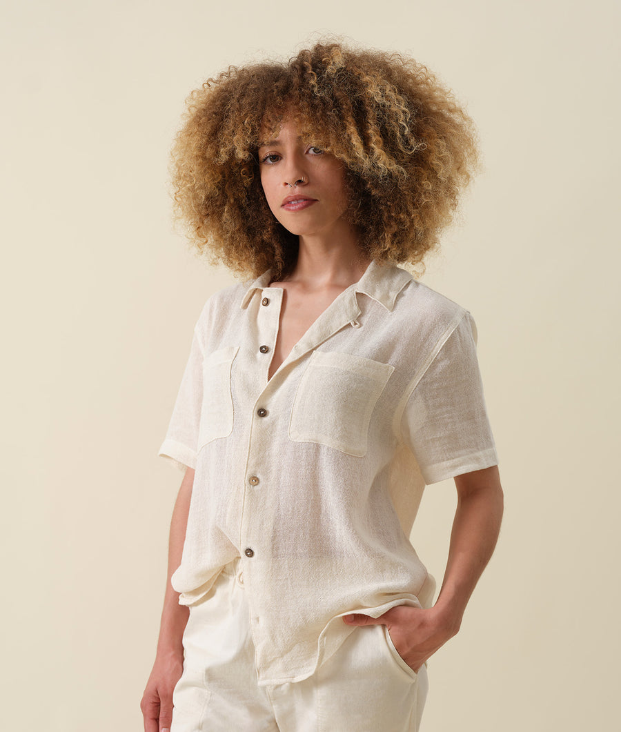Photograph of a woman wearing a relaxed-fit, off-white linen short-sleeve button-up shirt - Industry of All Nations