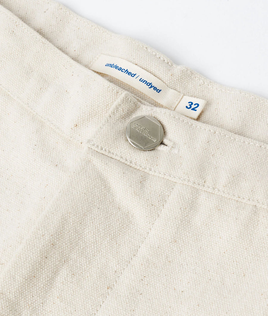 Close-up detail shot of a cream-colored organic cotton t-shirt with 'unbleached / undyed' tag and size 32 label - Industry of All Nations