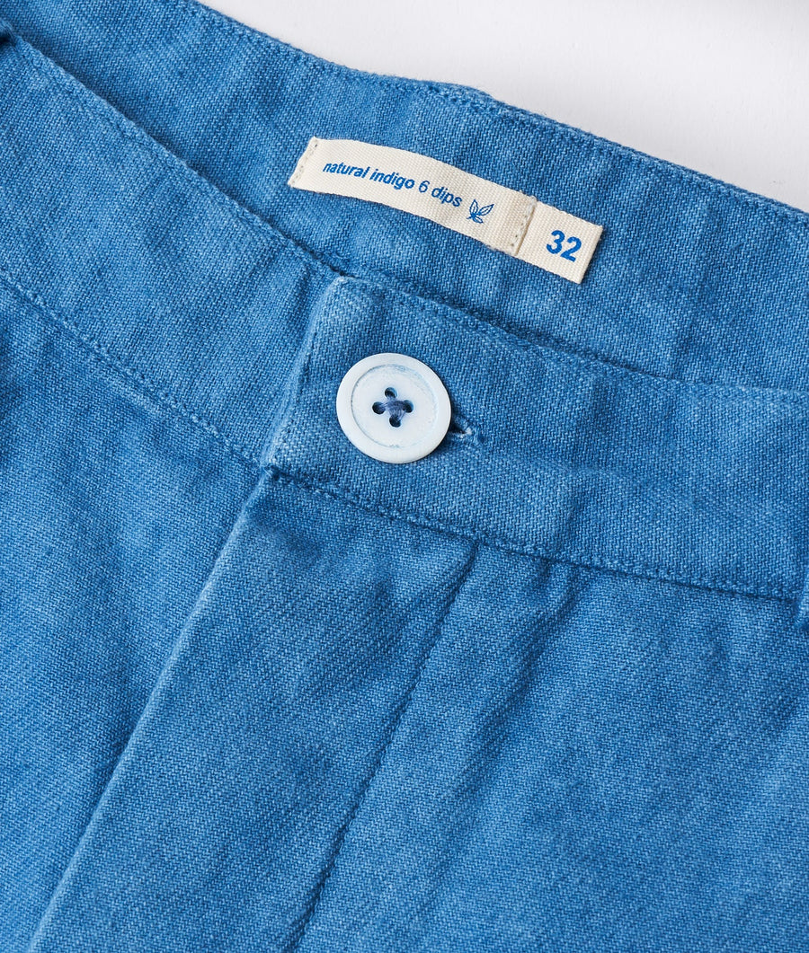 A close-up detail shot of a pair of blue cotton denim pants with a size 32 label and white button closure - Industry of All Nations