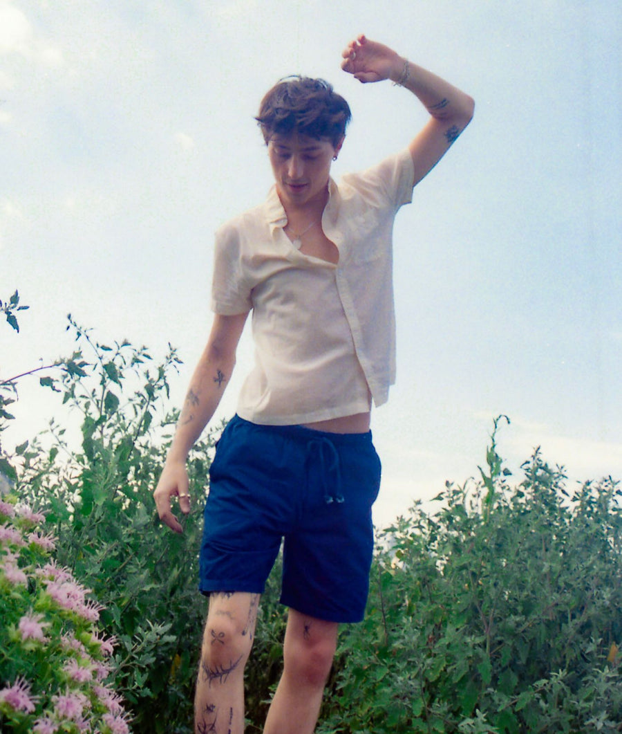 A person wearing a white top and blue shorts standing in a floral field - Industry of All Nations