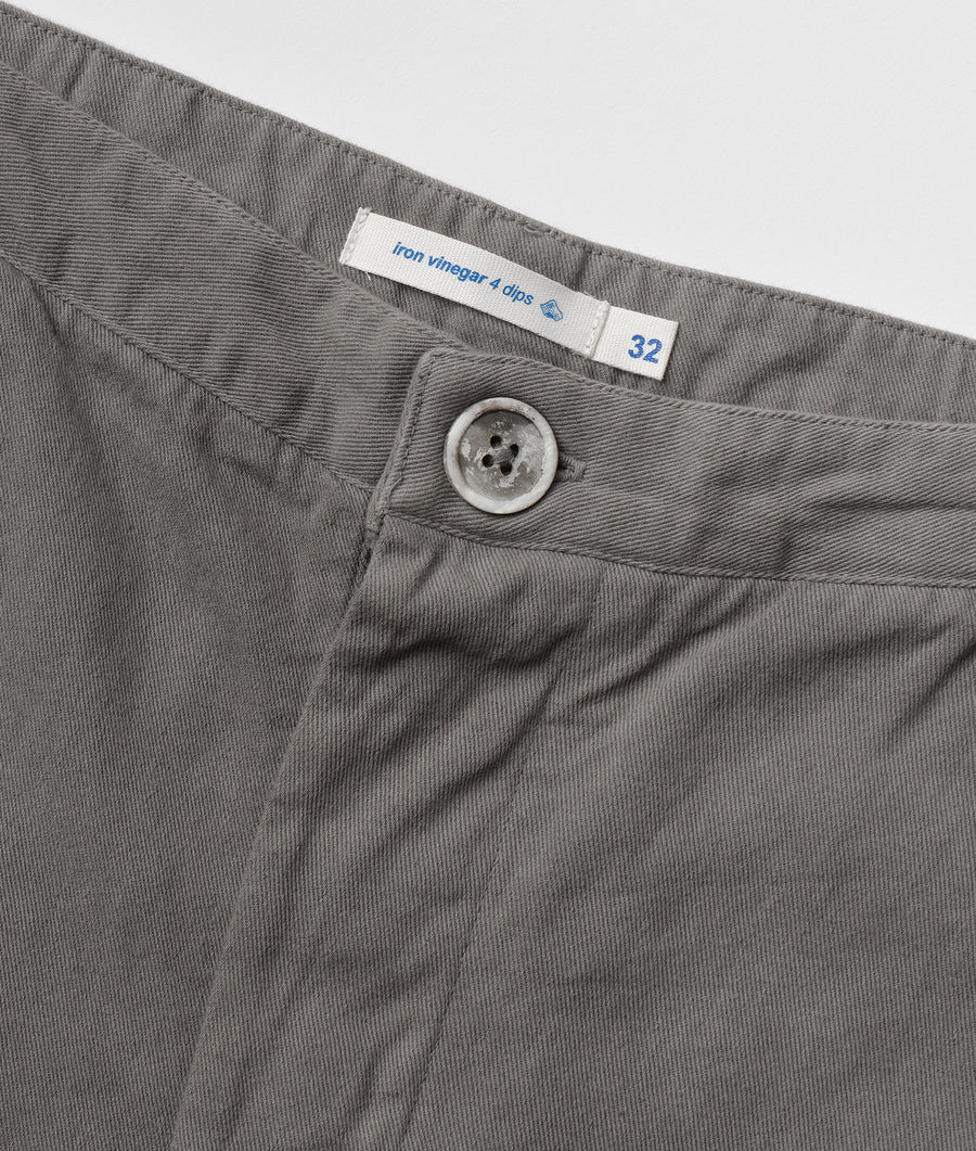 Close-up detail shot of a gray pair of trousers with an "Iron vinegar 4 clips" label and a white button closure - Industry of All Nations