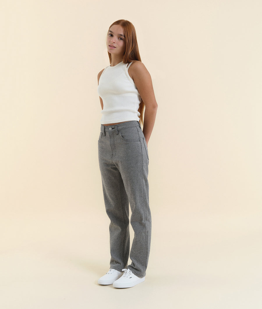 A young woman wearing a white ribbed knit tank top and grey high-waisted jeans, standing against a cream background - Industry of All Nations