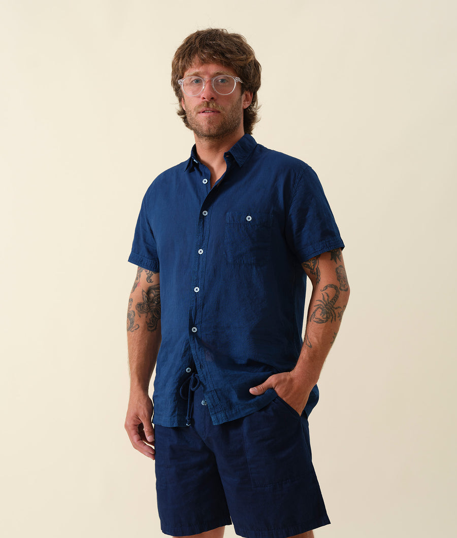 A man wearing a navy blue short-sleeve button-down shirt and navy blue shorts - Industry of All Nations