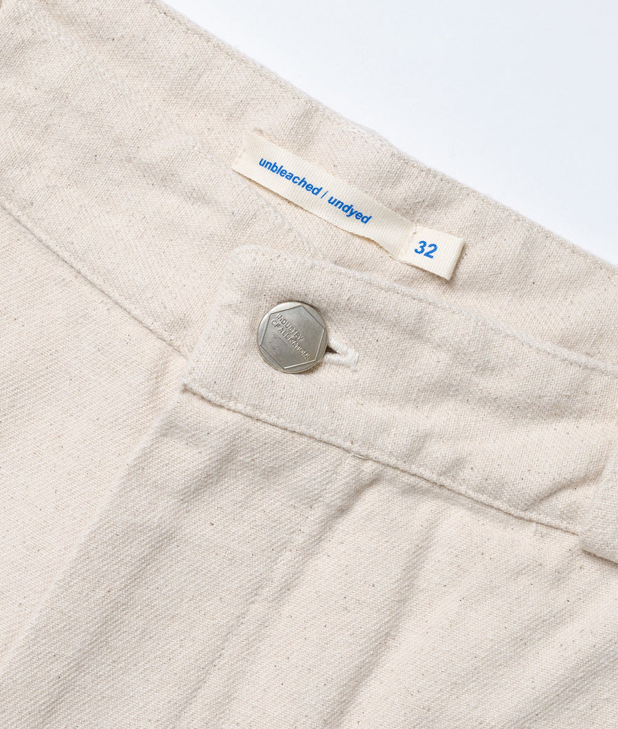 Flat lay photograph of a natural-colored, unbleached cotton garment with a size tag and a metal button - Industry of All Nations