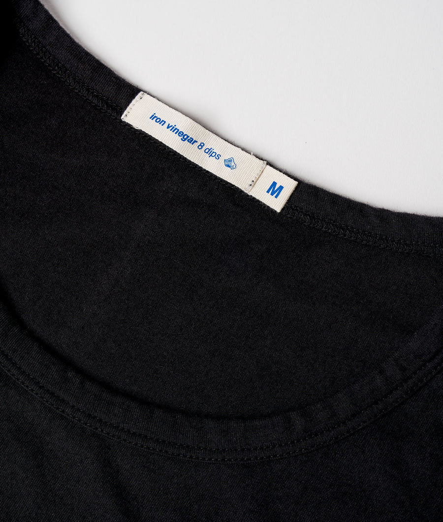 Detail shot of a black cotton t-shirt with a white garment tag that says "Iron Wingar & dlps" - Industry of All Nations