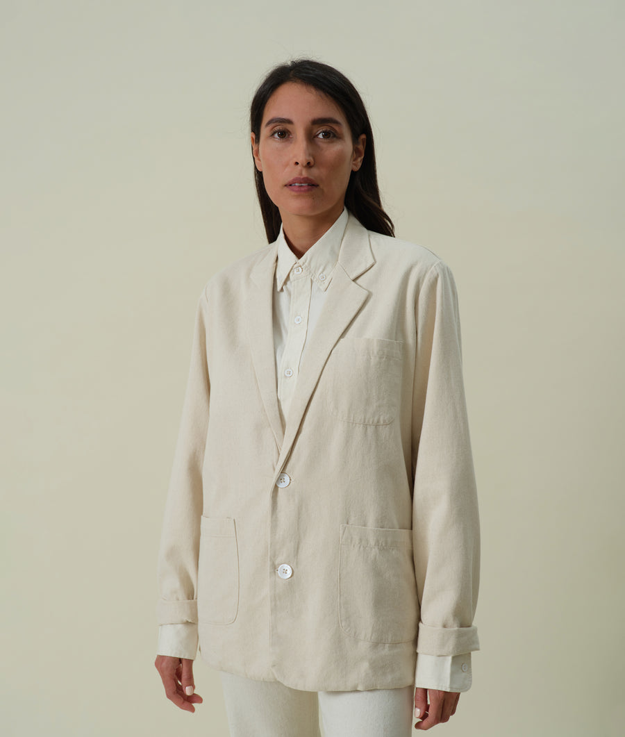 Portrait of a woman wearing a long, loose-fitting off-white linen blazer - Industry of All Nations