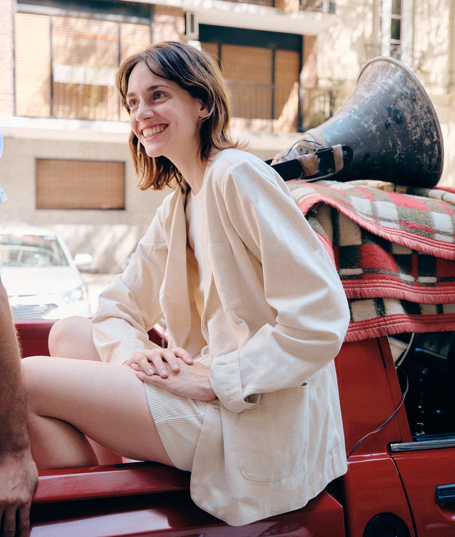 White oversized cotton jacket worn by a smiling woman sitting in front of a red vintage vehicle - Industry of All Nations