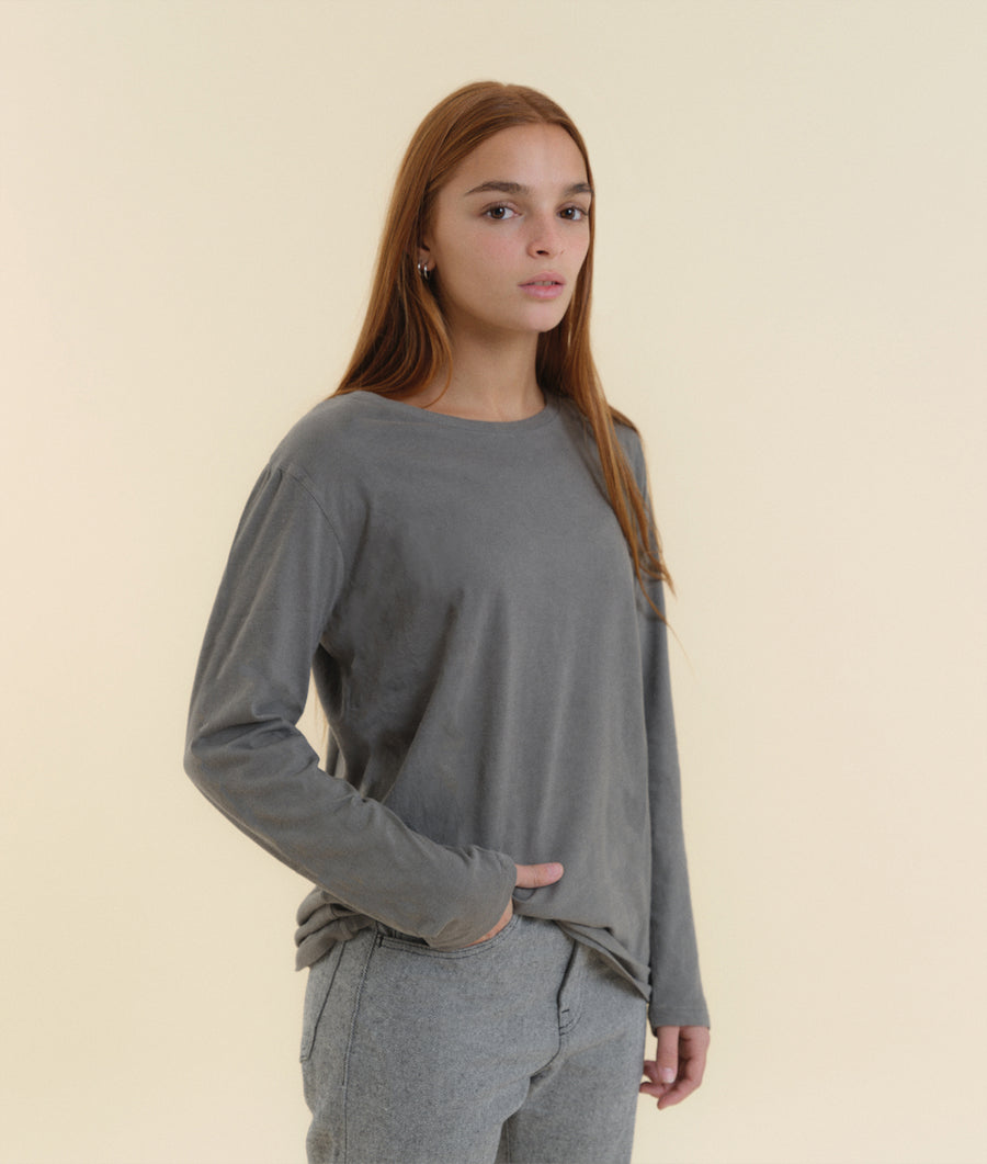 A young woman wearing a gray long-sleeved shirt against a neutral background - Industry of All Nations