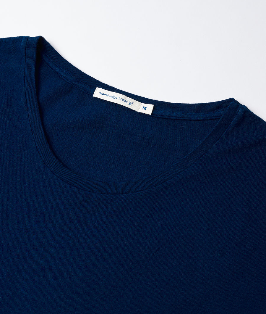 A navy blue t-shirt with a natural indigo label, displayed in a close-up detail shot - Industry of All Nations