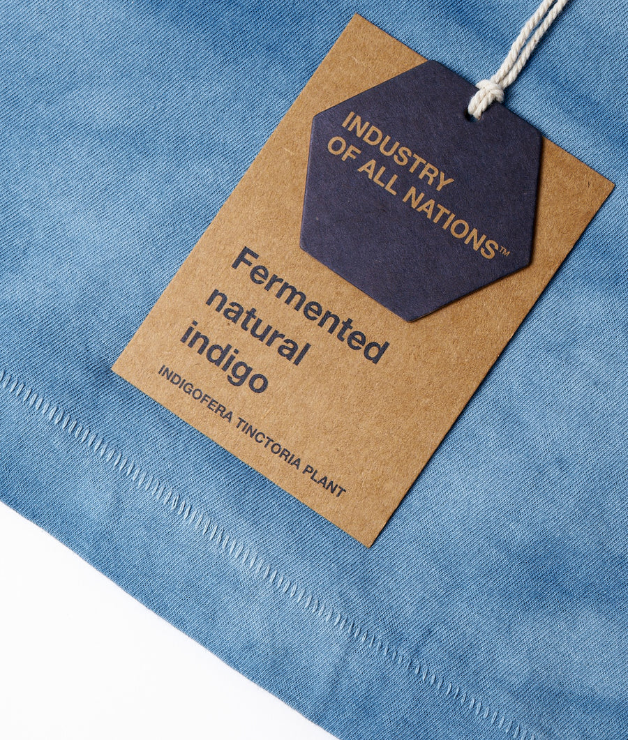 Fermented natural indigo fabric swatch displayed on blue denim background with "Industry of All Nations" branding - Industry of All Nations