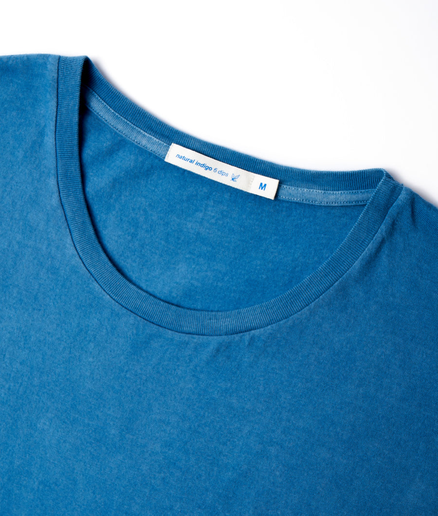 Closeup of a medium-sized, blue natural indigo cotton t-shirt with a ribbed neckline, displayed flat - Industry of All Nations