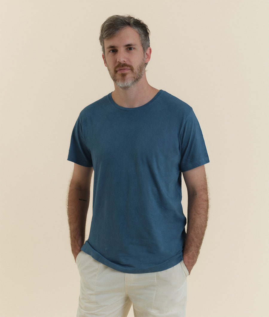 A man wearing a navy blue t-shirt and beige pants, standing against a neutral background - Industry of All Nations