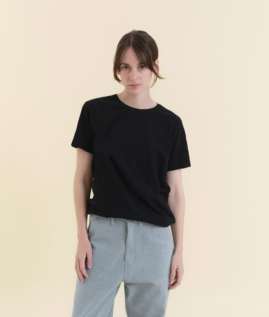 A woman wearing a black short-sleeved T-shirt stands against a neutral background - Industry of All Nations
