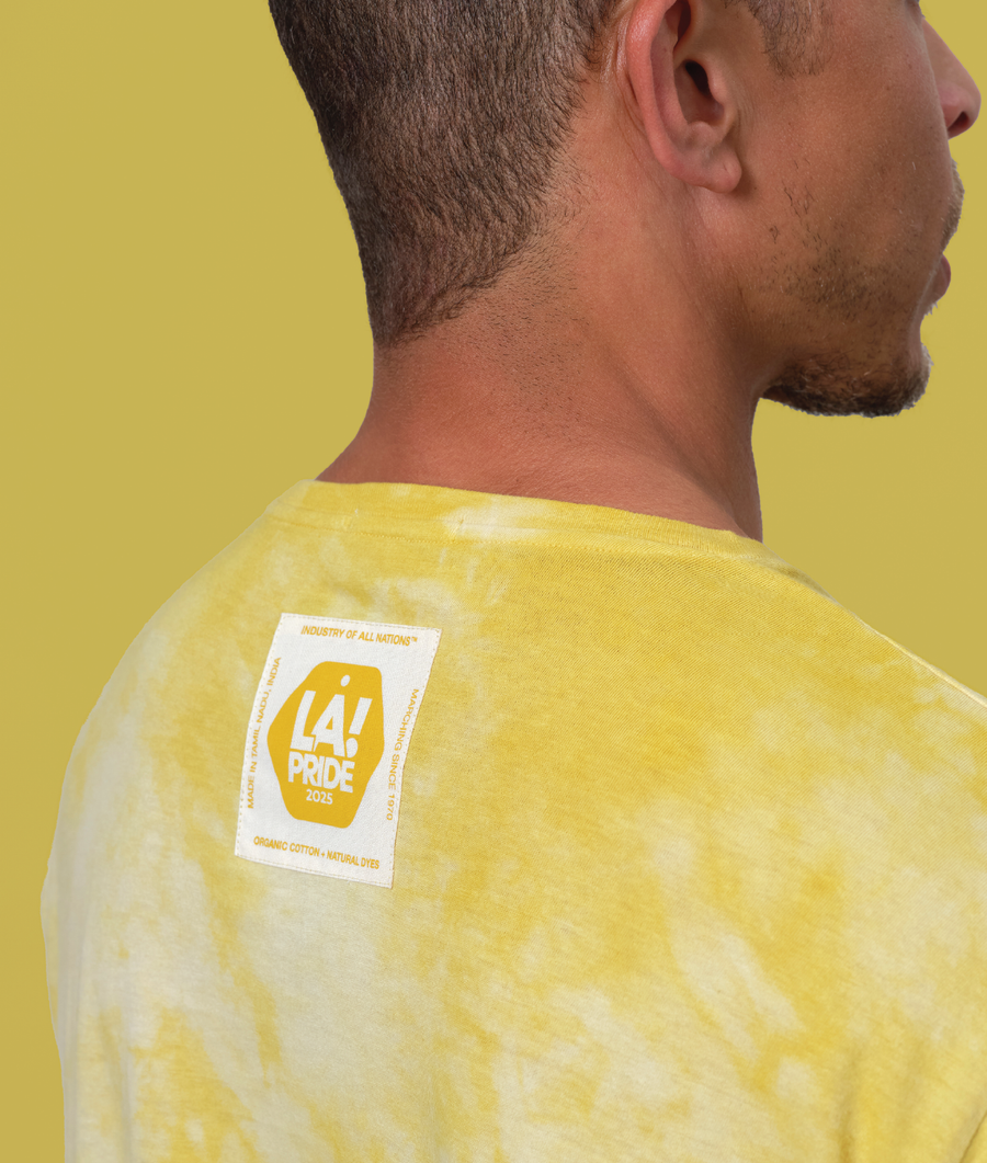 Close-up shot of a person wearing a yellow tie-dye t-shirt with an 'Industry of All Nations' logo patch - Industry of All Nations