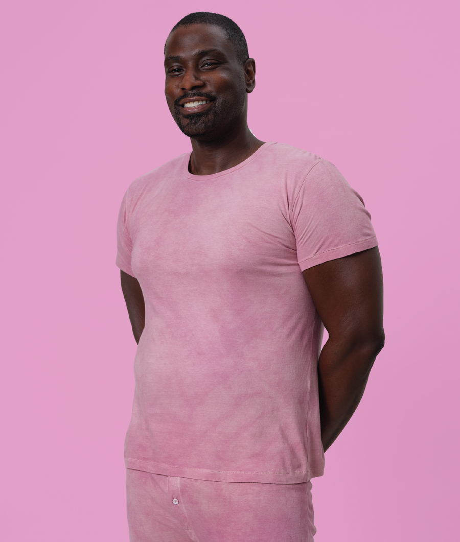 A smiling man wearing a light pink t-shirt against a pink background - Industry of All Nations