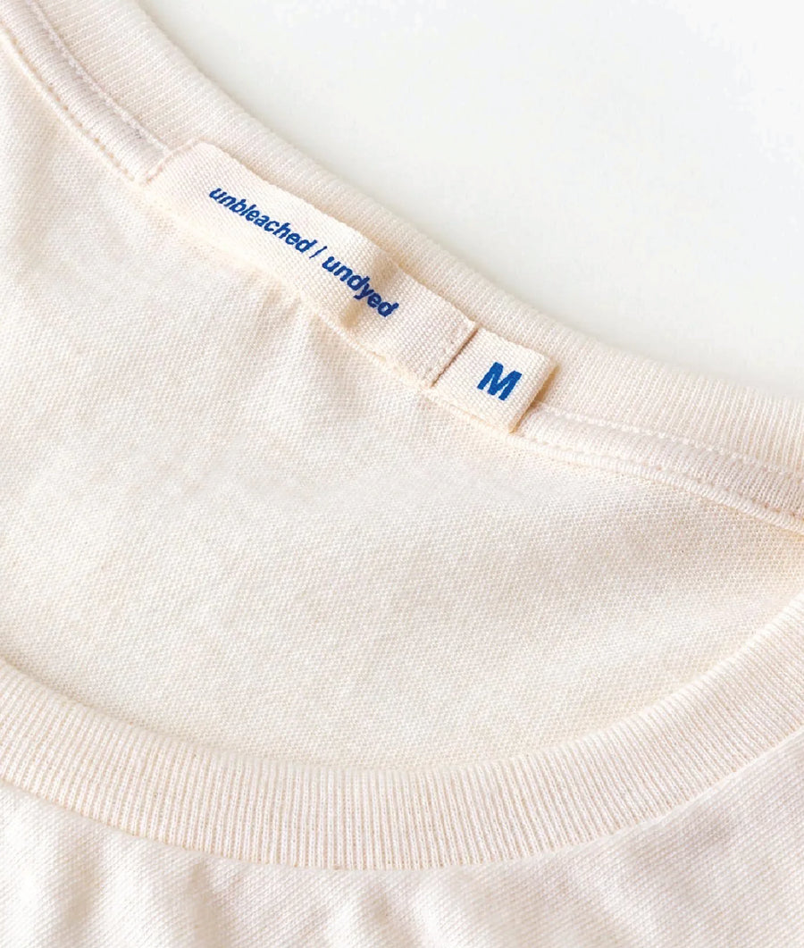 Detail shot of a white, unbleached, organic cotton t-shirt with the text "Unbleached I Undyed" printed on the tag - Industry of All Nations
