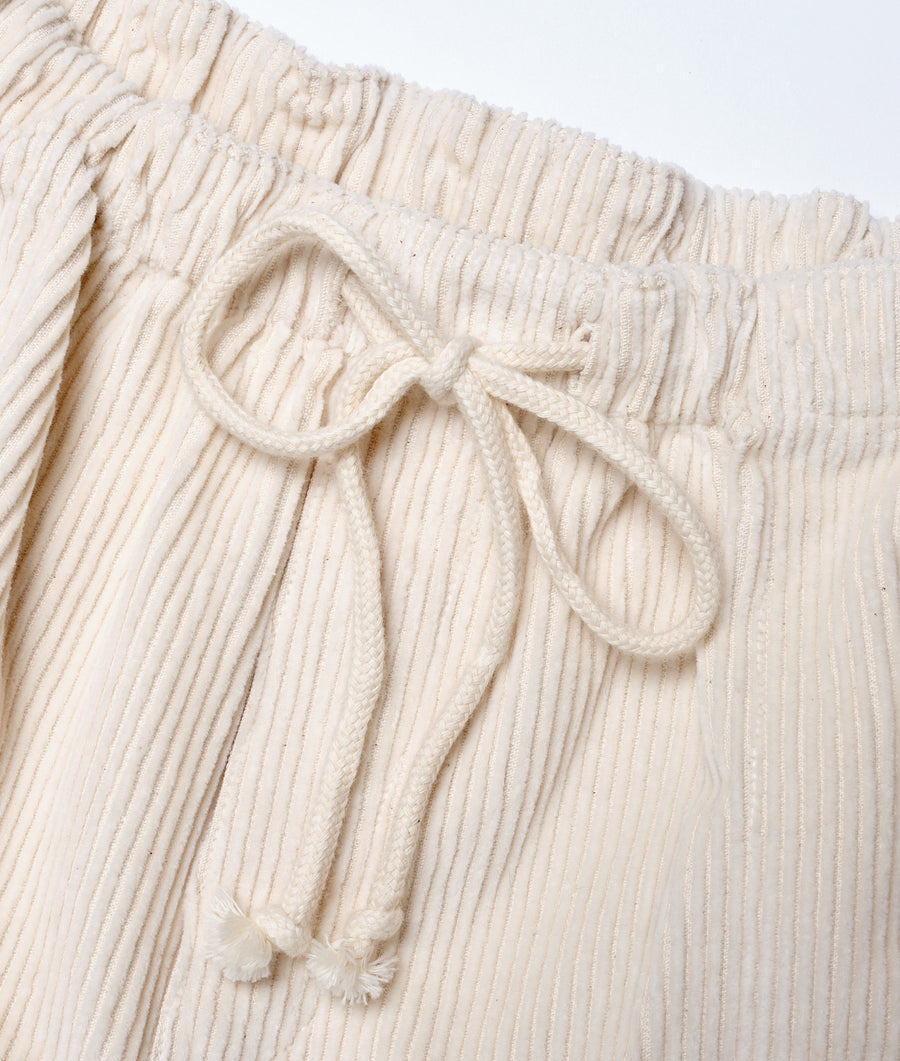 A close-up detail shot of a cream-colored cotton pleated skirt with a drawstring waist - Industry of All Nations