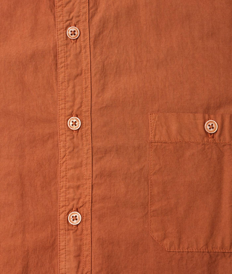 Detail shot of an orange, button-up shirt with four-hole buttons and a chest pocket - Industry of All Nations